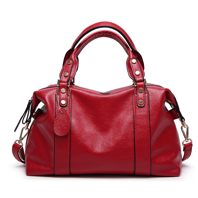 Red leather-style Boston handbag with top handles, gold hardware, and side zipper pull tabs.