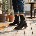 Black ankle boots on feet, side zipper and block heel, rounded toe, smooth upper