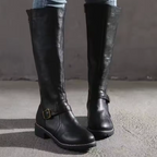 Black knee-high flat-heel boots with buckle strap across the upper.