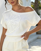 White one-shoulder batwing sleeve knit top with large floral applique at chest