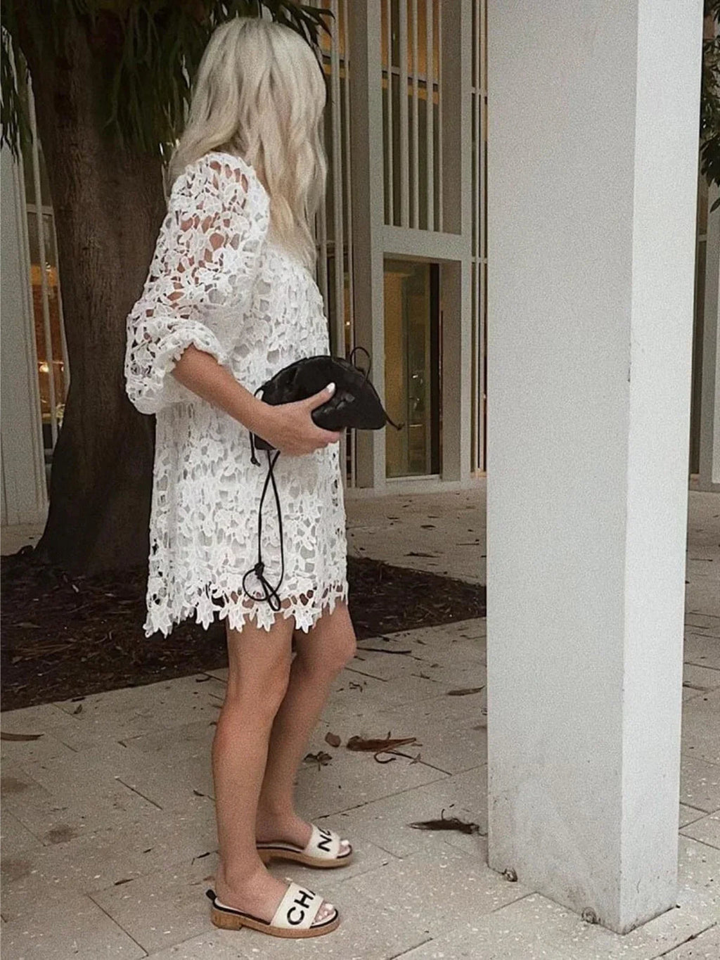 Braided faux leather drawstring bag held in hand; white lace dress wearer.