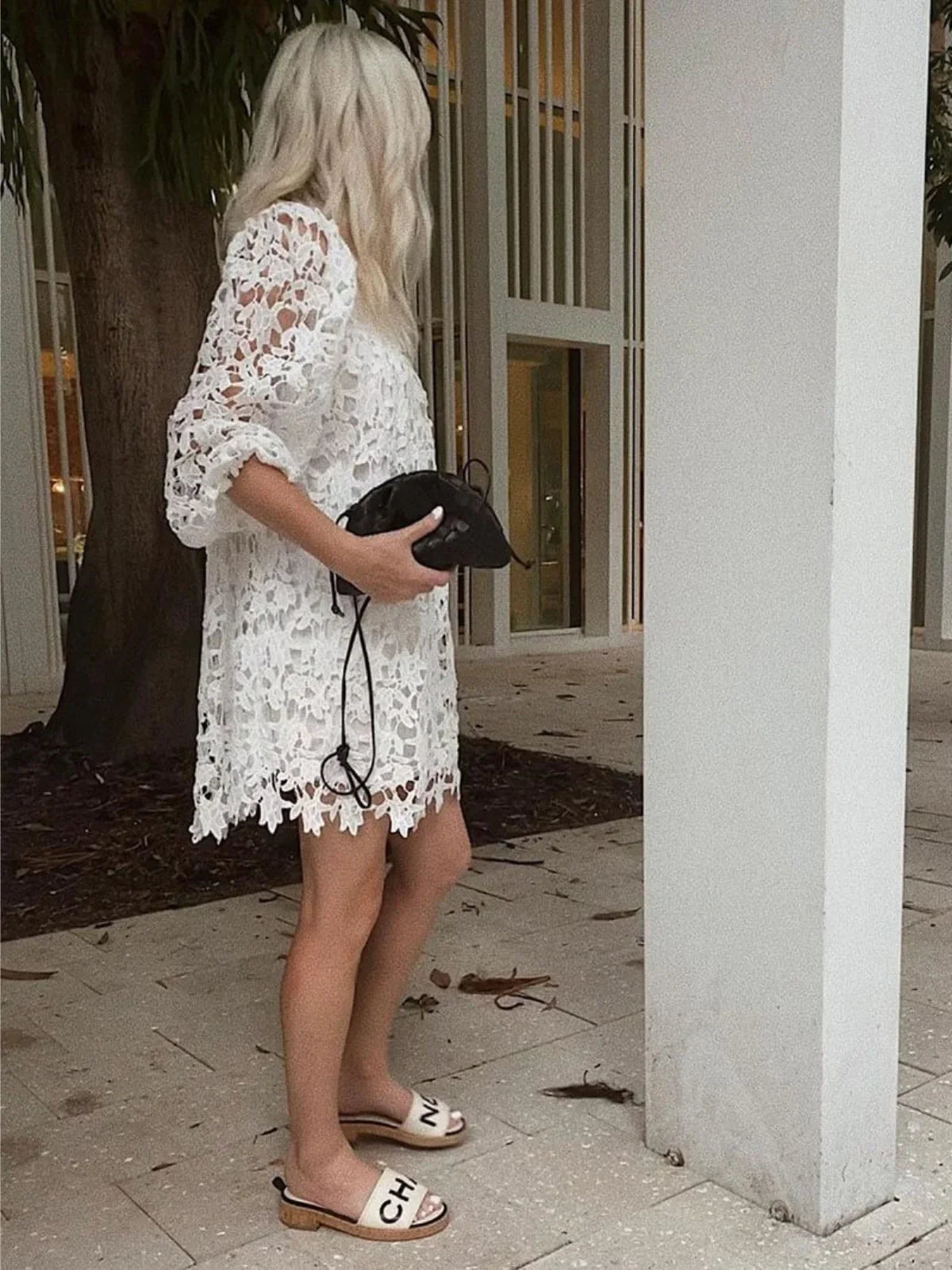 Braided faux leather drawstring bag held in hand; white lace dress wearer.