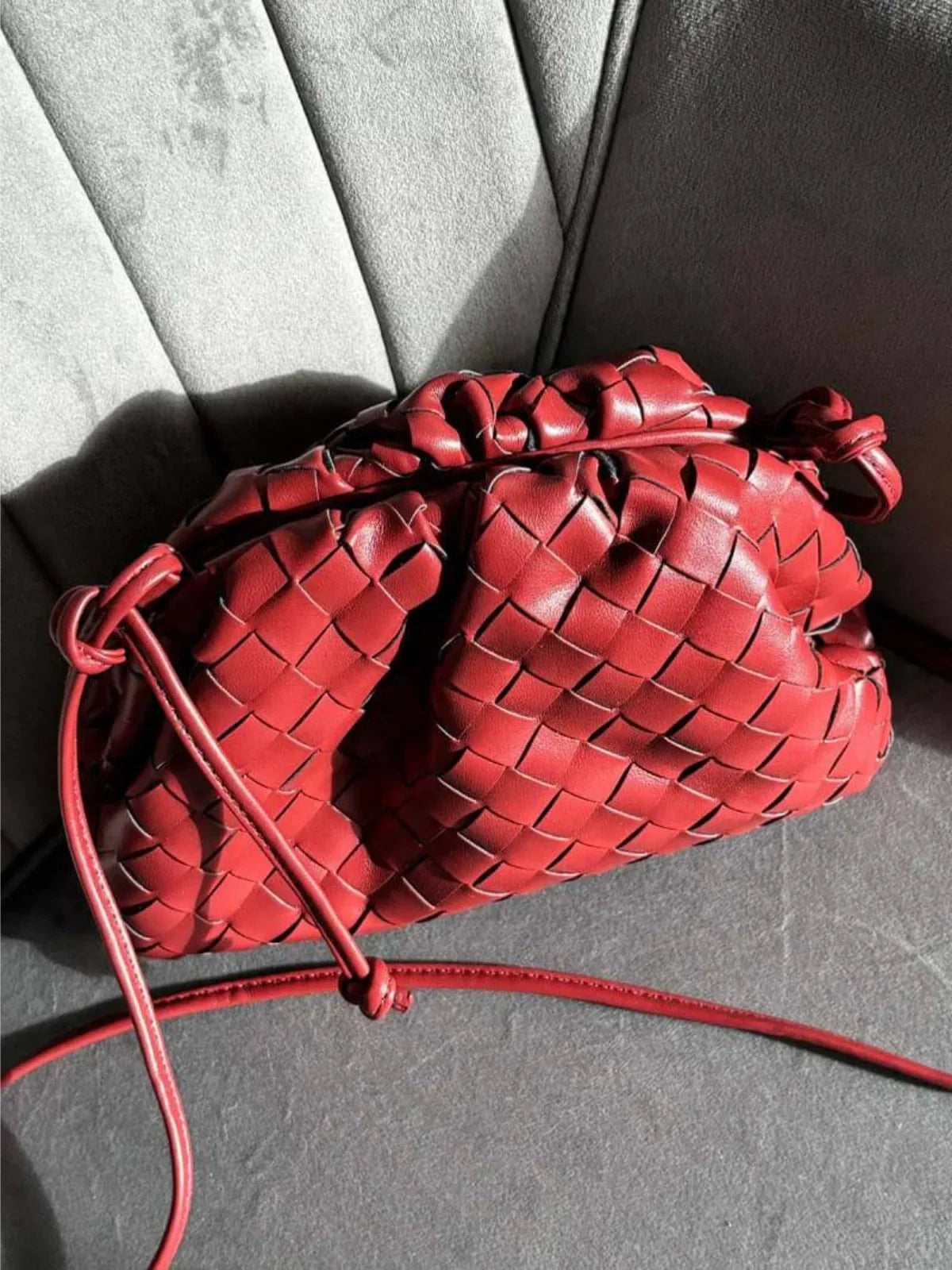 Red braided faux leather drawstring bag with cord draw closure and shoulder strap.