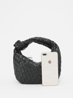 Black braided vegan leather crossbody bag with wide opening, phone placed inside.