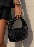 Black braided vegan leather crossbody bag with woven texture, held by the top handle.