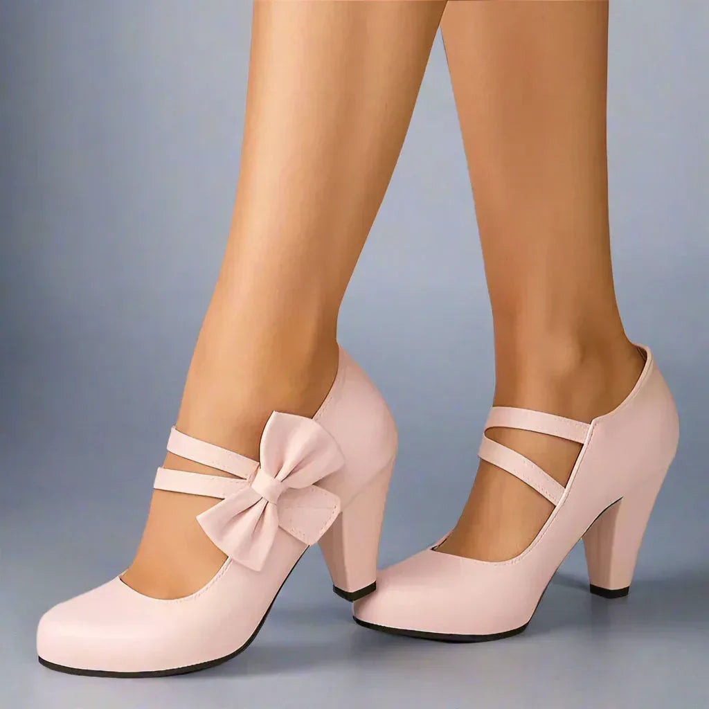 Pink bow detail heeled pumps, front view with ankle strap and mid-height heel
