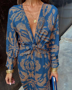 Blue patterned V-neck dress with tied waist knot and long sleeves, gold trim cuffs.