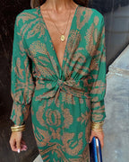 Green patterned V-neck midi dress with tied waist knot and long sleeves, gold cuff accents.
