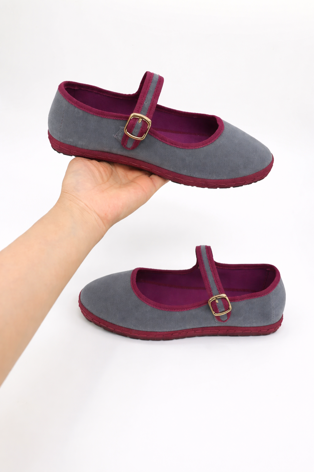 Gray Mary Jane flat with round toe and burgundy buckle strap, shown on a hand.