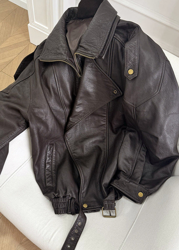 Women’s dark brown leather bomber jacket laid flat, zip front, snap pockets, belt strap