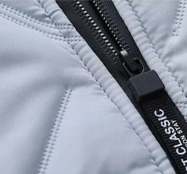 Close-up of zipper pull and stitched quilted panels on a light puffer jacket.