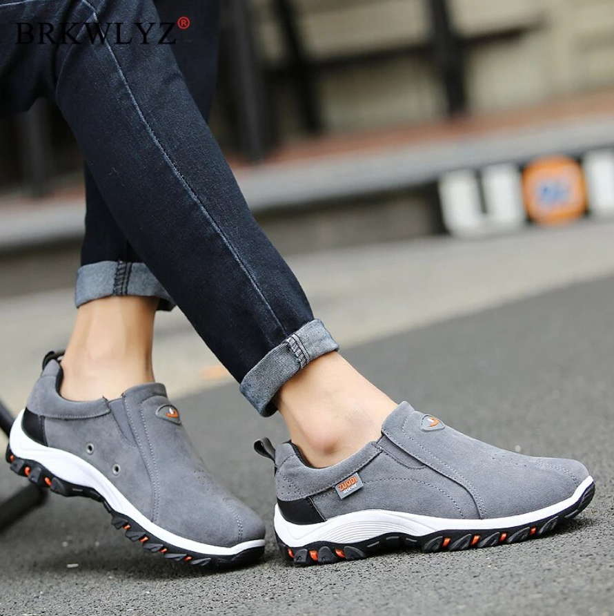 Men's gray hiking shoes on a sidewalk, slip-on style with white sole and orange grip