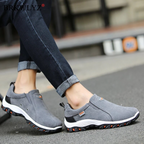 Men's gray hiking shoes on a sidewalk, slip-on style with white sole and orange grip