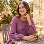 Women's relaxed peplum blouse in purple, crew neck, long sleeves with gathered cuffs.
