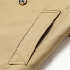 Beige trench coat fabric detail with stitched welt pocket and metal button