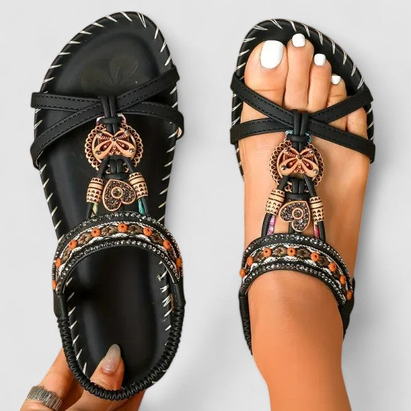 Black orthopedic cushioned strap sandals with crisscross straps and ornate hanging charms