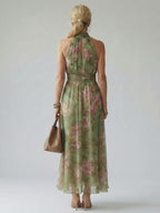 Back view of women’s sage green floral halter midi dress with gathered waist seam