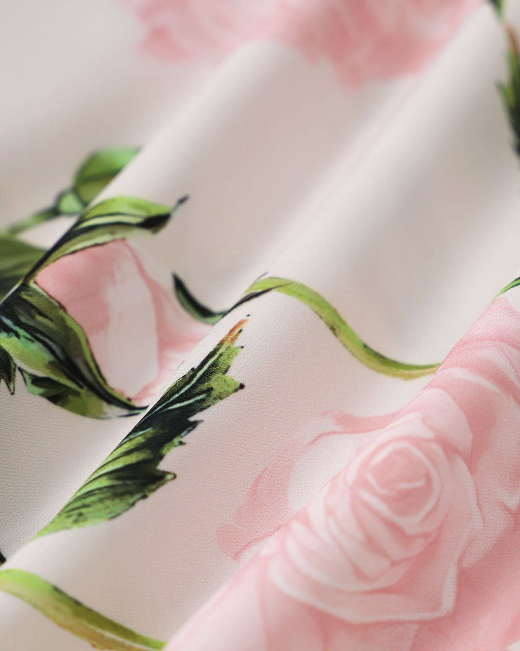 Close-up floral print fabric: pink roses and green leaves on white