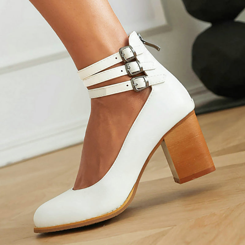 White triple-buckle block heel ankle strap pumps, close-up of three buckle straps.