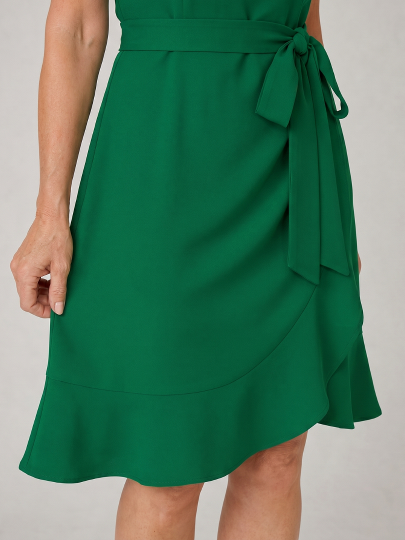Green mini dress close-up showing side tie bow and layered wrap-style skirt panel
