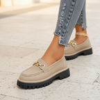 Beige slip-on loafers with gold chain detail, buckle strap, and rugged chunky outsole
