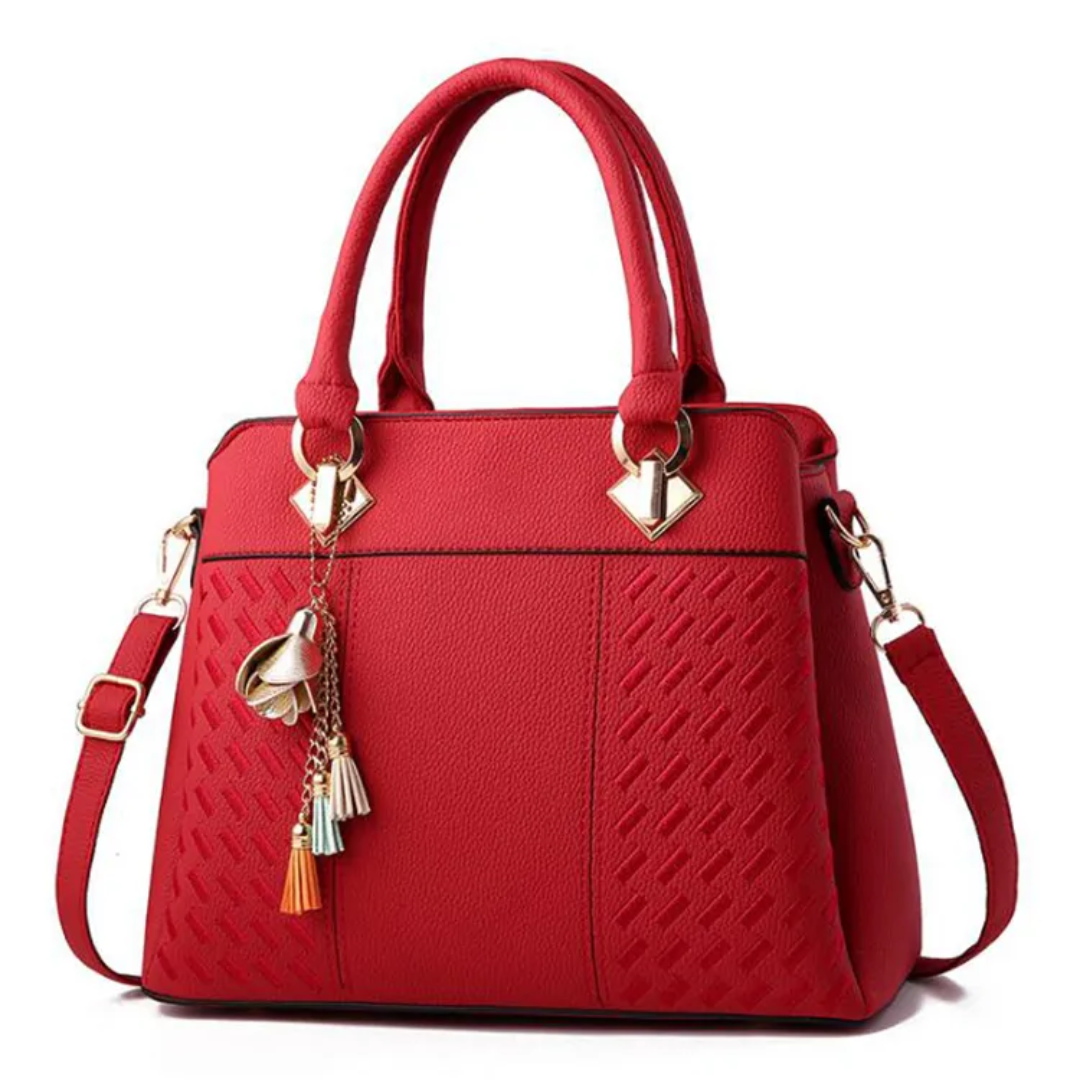 Red textured shoulder bag with top handles, tassel charms, gold-tone hardware, crossbody strap