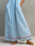 Blue striped maxi dress close-up: gathered skirt and red-trim border at hem