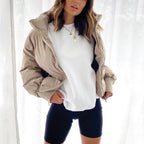 Beige short puffer jacket with hood and full zipper, worn over a white top