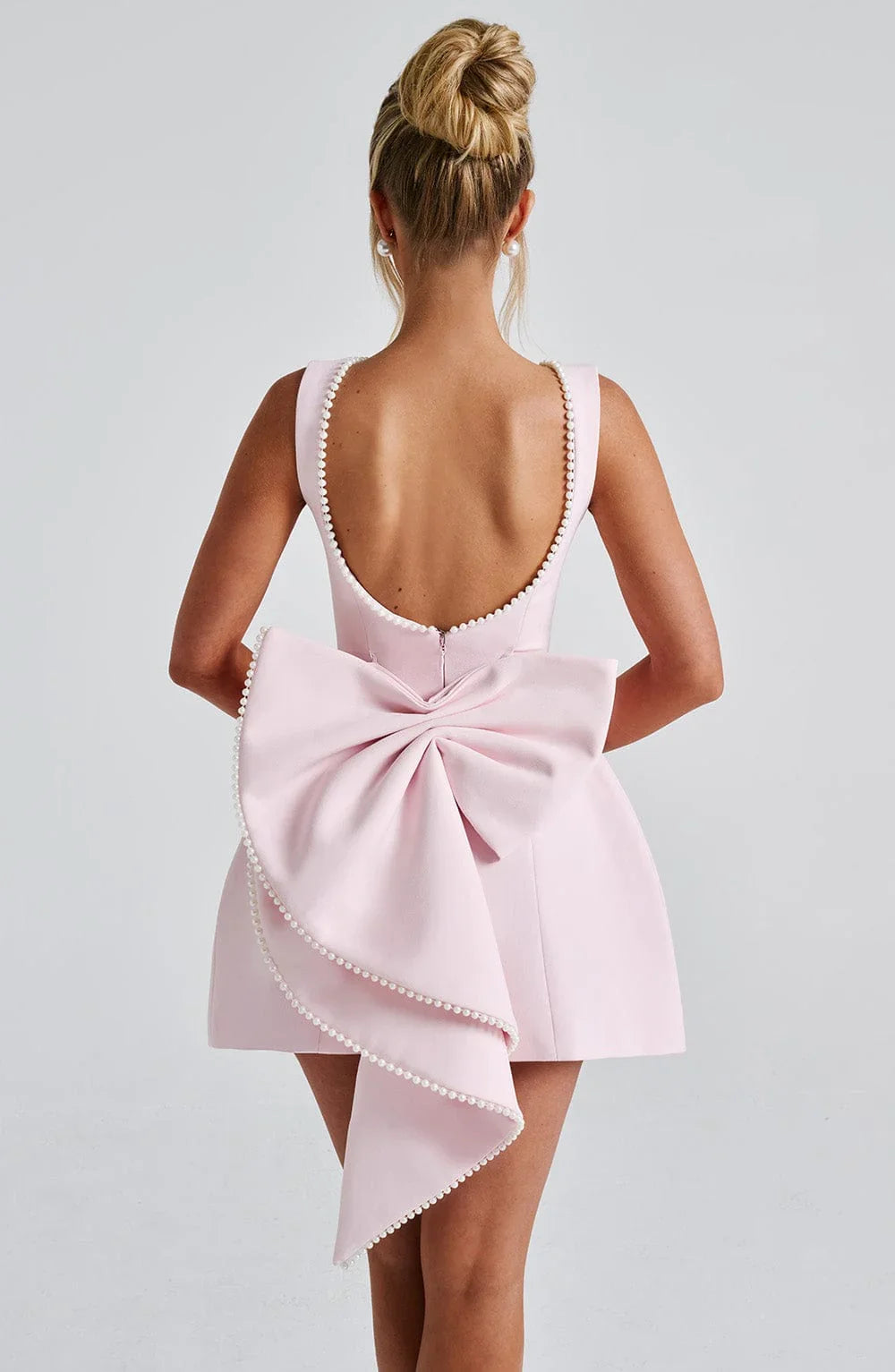 Back view of blush pink sleeveless mini dress with pearl trim and bow detail