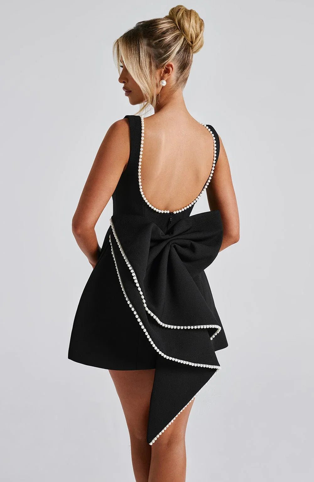 Back view of black sleeveless mini dress with pearl trim and large bow