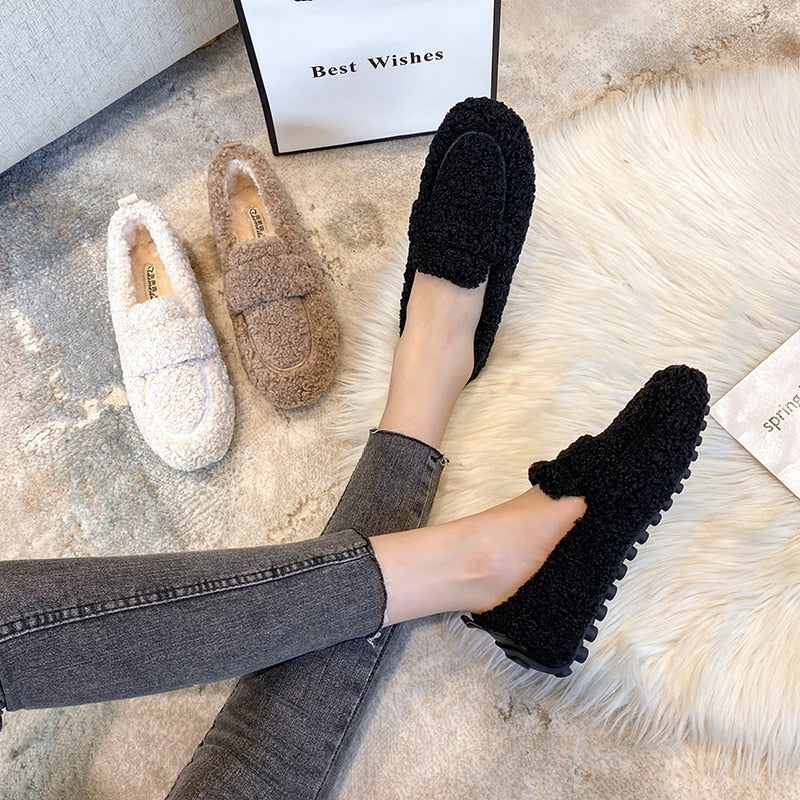 Women’s black fleece teddy slip-on slippers, shown with tan pair nearby