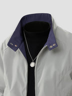 Light gray jacket close-up with full-zip front, snap collar, and buttoned shoulder tabs.