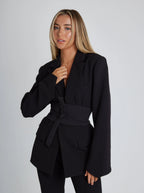 Black tailored blazer with wide belt, structured shoulders, long sleeves, flap pockets
