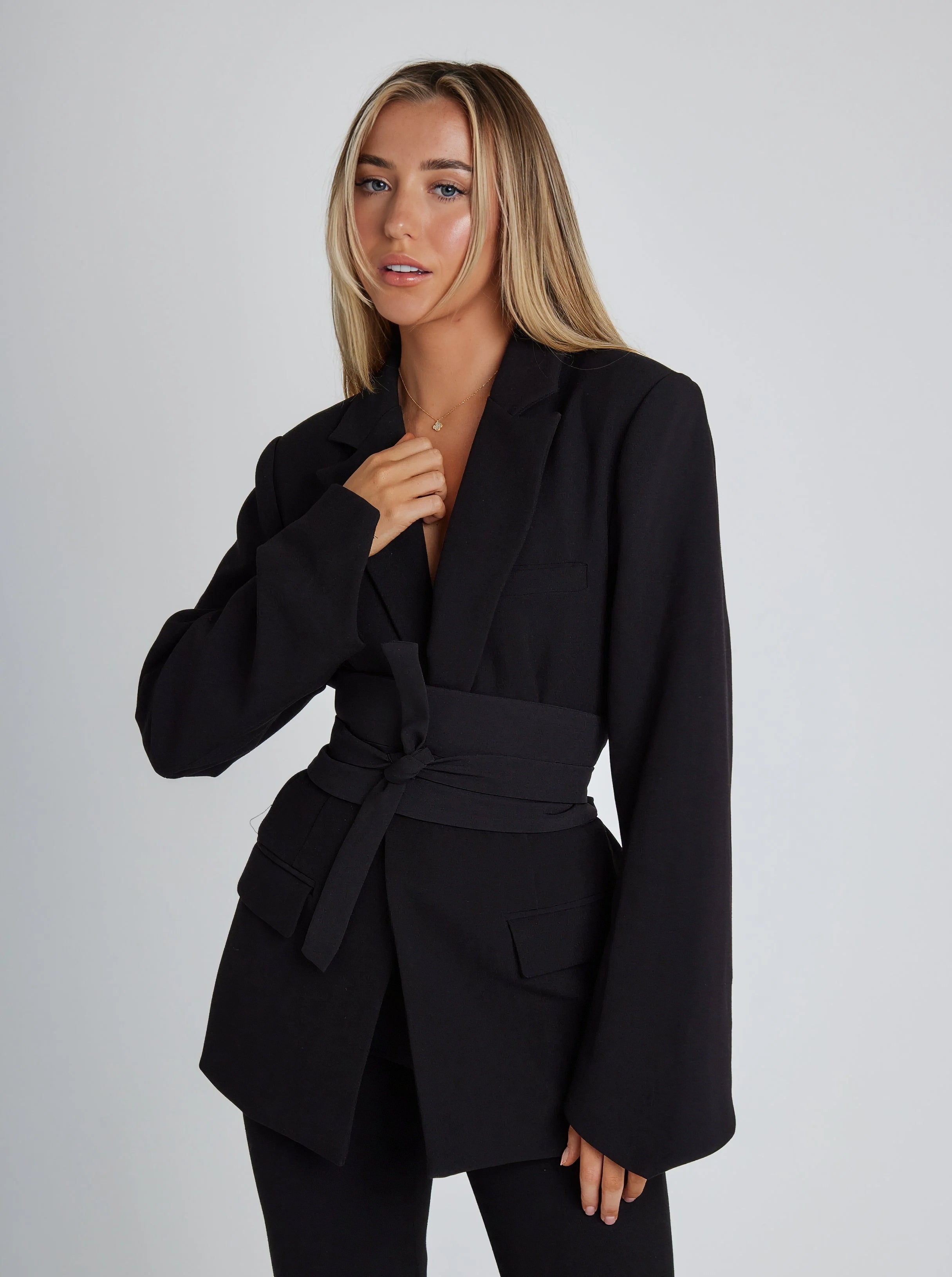 Black tailored blazer with wide belt, structured shoulders, long sleeves, flap pockets