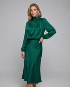 Dark green satin midi dress with long sleeves and high neck, one hand on hip.