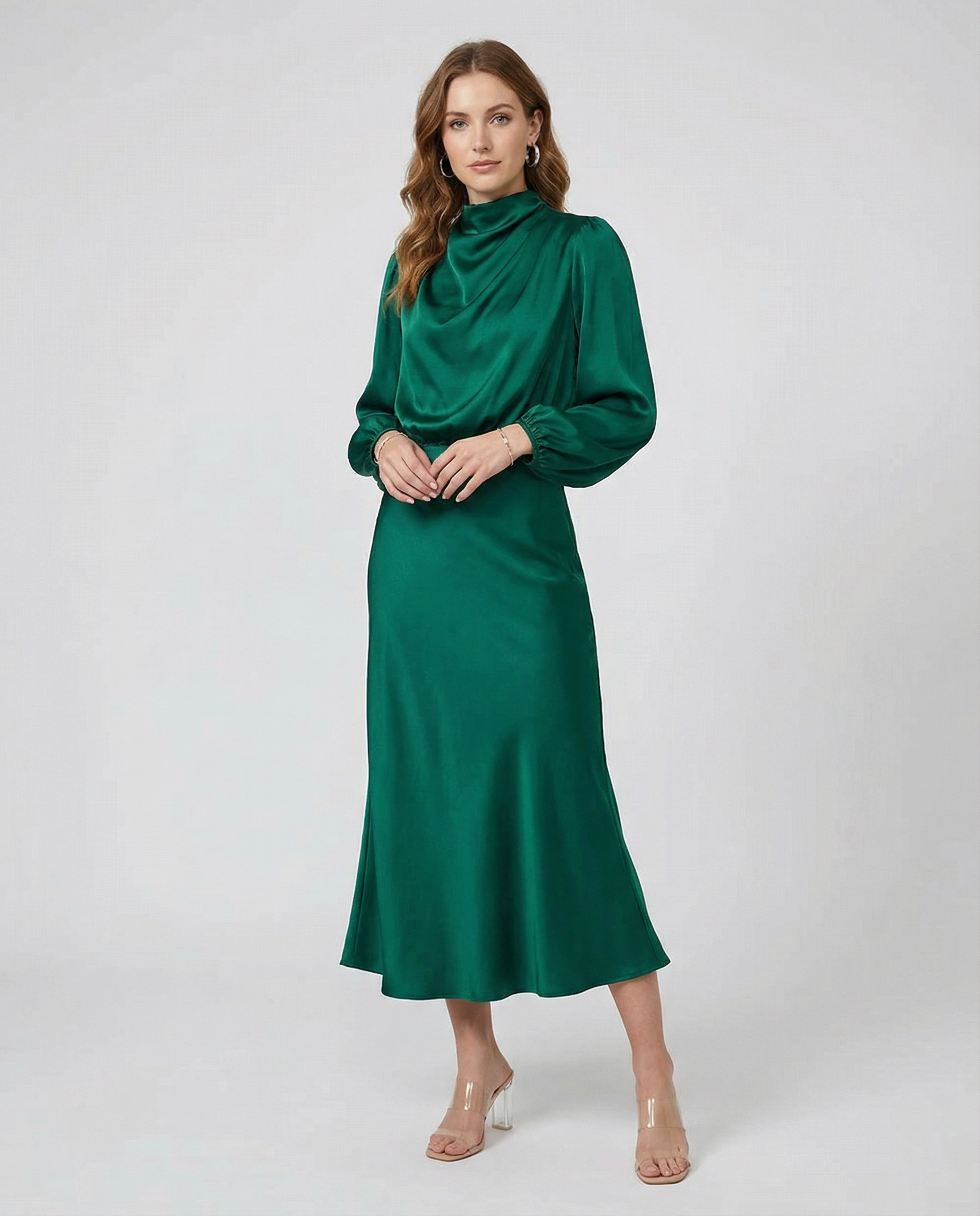 Emerald green satin midi dress with long sleeves and high neck, hands clasped front.