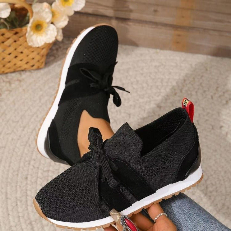 Women's black knit slip-on sneakers with lace-up bows and white rubber sole.