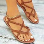 Brown open-toe flat sandals with crisscross braided straps and gold ankle chain