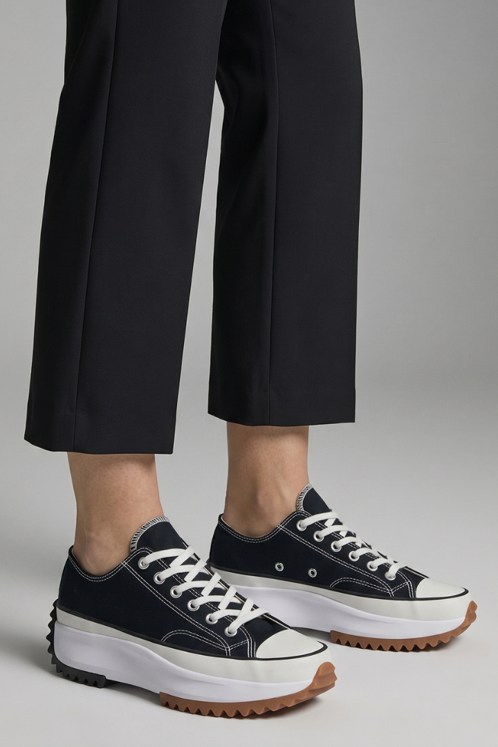 Women’s black trainers with white midsoles and leather platform sole, side view