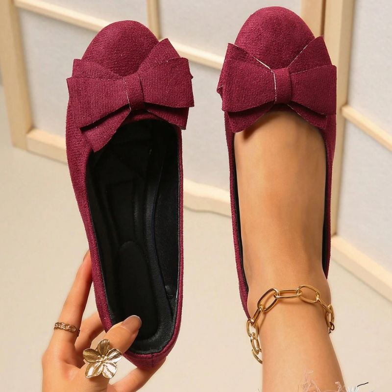 Dark red cushioned ballet flats with suede bow and gold chain ankle strap