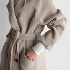Beige belted coat close-up with tie waist, front pockets, and button placket